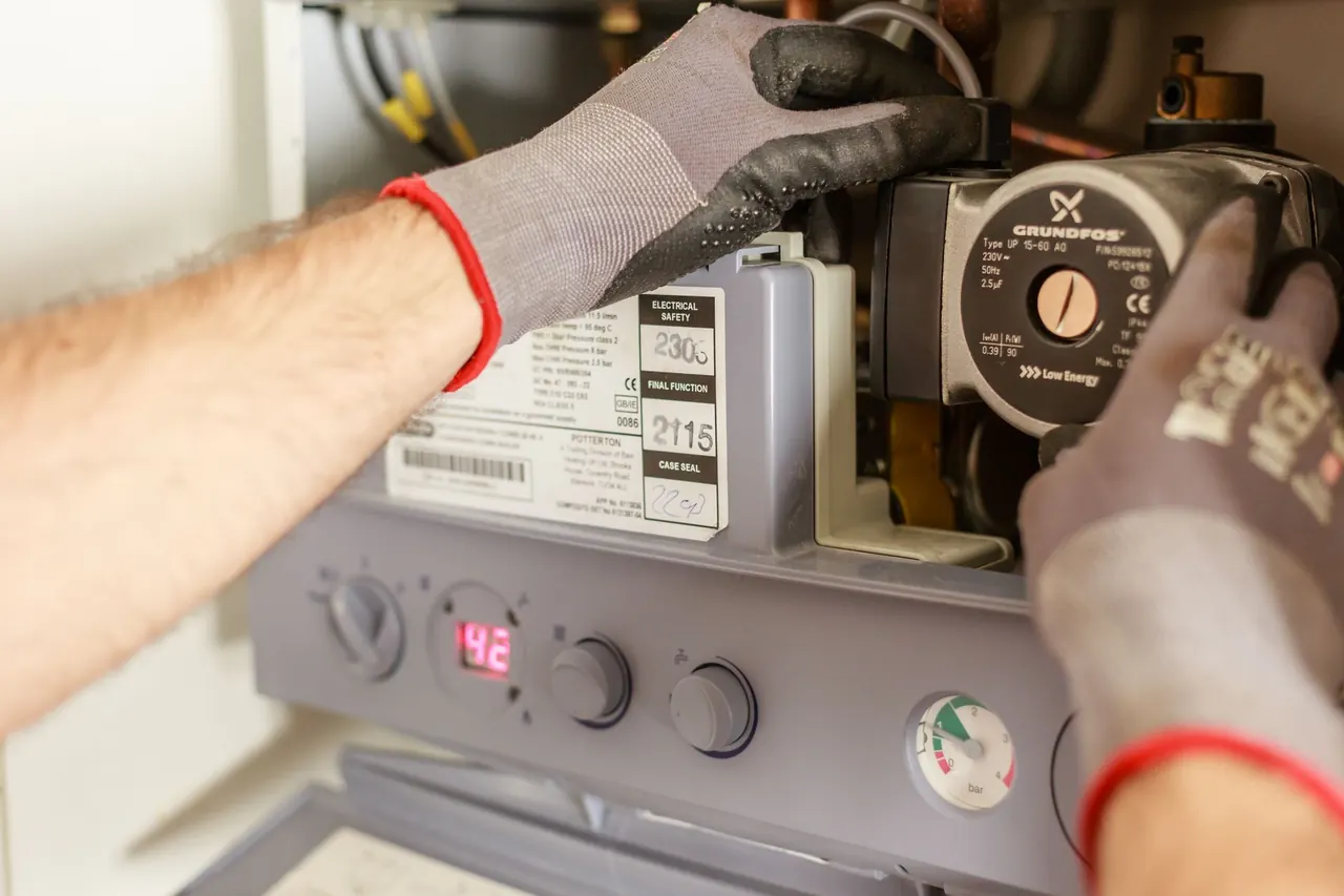 Gloved technician working beside a boiler control panel and circulation pump